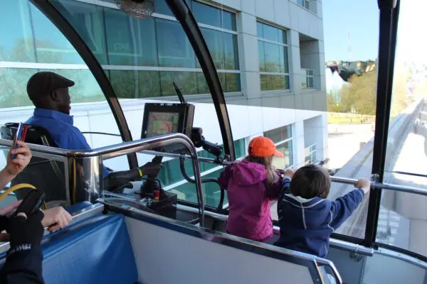 A family with small children riding the Seattle Center Monorail to Seattle Center. Two small kids are riding next to the train engineer in the front row seat next to the window.