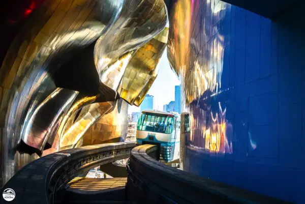 Seatle Center Monorail Train Travelling Through Tunnel in design of the MOPOP Building Near Seattle Center to Represent Why Locals Love The Seattle Monorail.